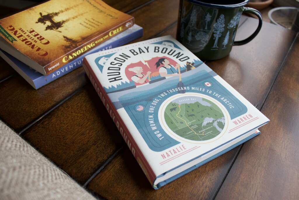A book "Hudson Bay Bound" sits on a dark colored table. Two other books are stacked in the background.
