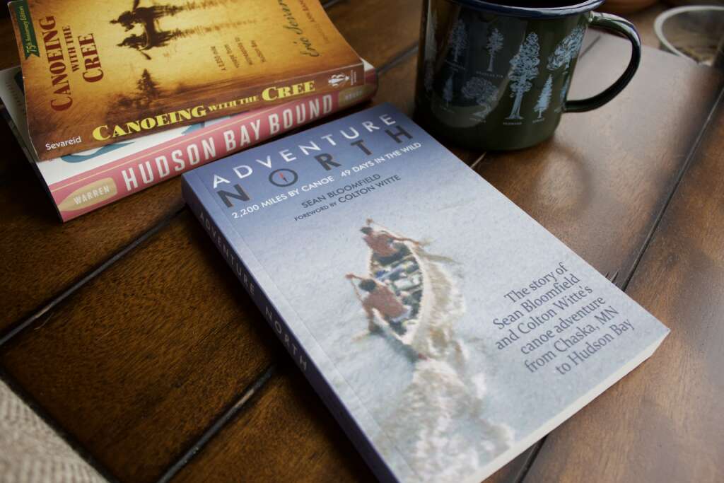 A book "Adventure North" sits on a dark colored table. Two other books are stacked in the background.